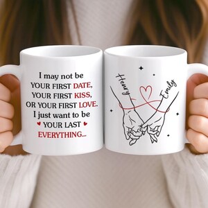 Könnte beinhalten: Zwei weiße Keramikbecher mit schwarzem Text und Illustrationen. Auf einem Becher steht: „Ich bin vielleicht nicht dein erstes Date... Ich möchte einfach dein letztes ALLES sein...“ Der andere Becher zeigt zwei Hände, die sich halten, mit den Namen „Henry“ und „Emily“.