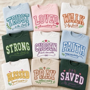 May include: Nine crewneck sweatshirts in various colours, each featuring embroidered collegiate-style lettering and religious phrases including Trust in the Lord, Loved, Walk by faith, Strong, Chosen, Faith moves mountains, Blessed, Pray, and Saved by grace.