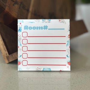 May include: A square notepad with a white background featuring a repeating pattern of medical-themed illustrations. The top center displays the text Room# followed by a line. Below are five red checkboxes each aligned with a horizontal red line.