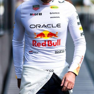 Peut inclure: Un haut blanc à manches longues et un pantalon bleu marine avec des logos de sponsors, dont "Oracle" et "Red Bull". La personne porte une casquette bleu marine avec le numéro "1" et le logo "Oracle Racing".