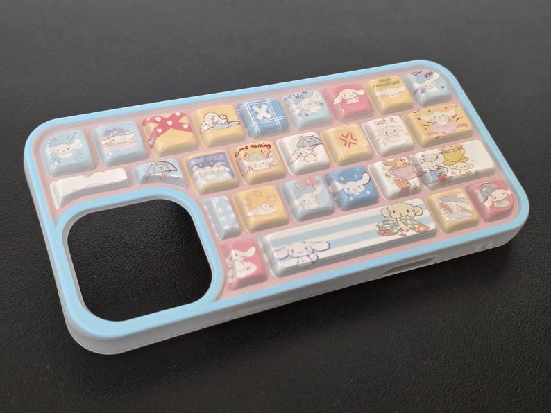 May include: A light blue phone case with a keyboard design. The case features a series of colorful, square keys with cartoon character illustrations. The keys are in shades of yellow, pink, blue, and white. The case has a rounded edge and a cutout for the phone's camera.