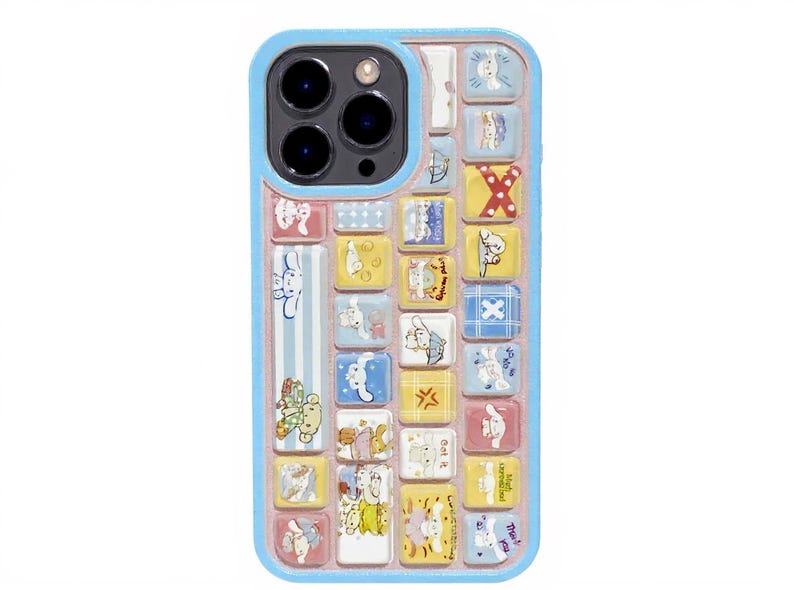 May include: A blue phone case with a keyboard-like design featuring cartoon characters. The case has a light blue border and a pink interior. The keyboard keys are yellow, blue, and white, with various cartoon illustrations.
