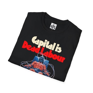 May include: Black t-shirt with the text "Capital is Dead Labour" in white and red. The graphic depicts a muscular figure in a mask, connected to wires. The shirt has a crew neck and a small tag near the collar.