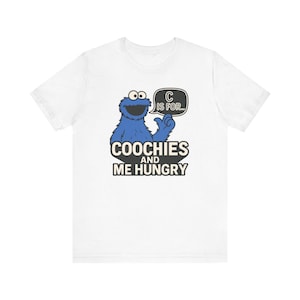 May include: White t-shirt featuring a blue cartoon character with the text "C is for..." in a speech bubble. Below the character, the shirt reads "Coochies and Me Hungry" in a black and white design. The shirt is made of a soft material.
