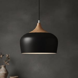 May include: A modern pendant light with a black, rounded shade and a natural wood top. The light hangs from a thin black cord, illuminating the space below. The fixture has a minimalist design.