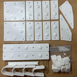 May include: An assortment of white plastic components, including rectangular and square pieces with raised circular details, and curved brackets. Some pieces have the text "tempco 450" and "DCI Products" printed on them. A clear plastic bag contains additional small white squares.