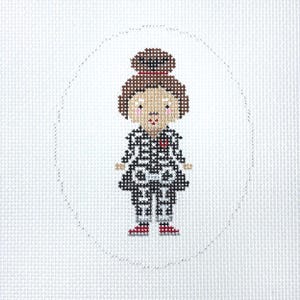 May include: A cross-stitch embroidery on white fabric featuring a stylized figure with a brown hair bun, pink cheeks, and a black and white skeleton-patterned outfit with a small red heart detail on the chest, enclosed in a stitched oval border.