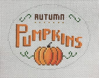 May include: A needlepoint canvas with an orange pumpkin and the text "Autumn Pumpkins" in a brown circle.