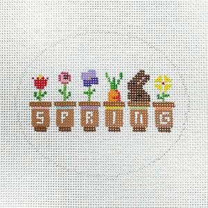 May include: A needlepoint canvas with a circle design featuring six potted plants spelling out the word "SPRING". The plants include a red tulip, a pink flower, a purple flower, a green plant with a carrot, a brown bunny, and a yellow flower.