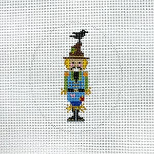 May include: A whimsical scarecrow with a black crow on its hat, wearing a blue shirt, brown pants, and a straw hat. The scarecrow is holding a small red apple in its hand.
