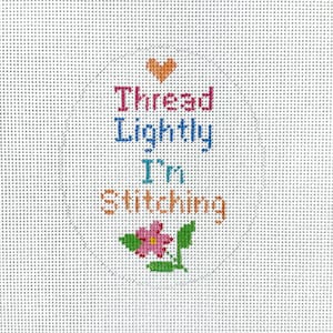 May include: A white canvas with a colorful cross-stitch design. The design features a pink flower with green leaves and the text "Thread Lightly I'm Stitching" in pink, blue, and orange.