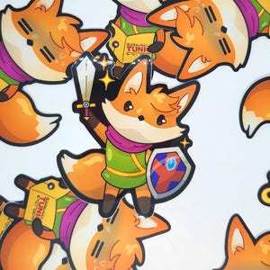 May include: A collection of stickers featuring a cartoon fox character in a green tunic, purple scarf, and holding a sword and shield. The fox has orange fur and is surrounded by star accents. Some stickers have the word "TUNIC" on them.