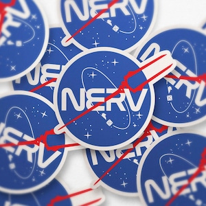 Könnte beinhalten: Eine Sammlung runder Aufkleber mit blauem Hintergrund und dem Wort "NERV" in Weiß. Die Aufkleber zeigen ein weißes Oval mit einer roten Linie und Sternen. Die Aufkleber sind auf einer weißen Oberfläche verstreut.