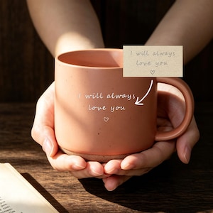May include: A terracotta-colored ceramic mug with a speckled finish and a rounded handle. The mug features the white printed text "I will always love you" followed by a small heart outline. A rectangular card above displays the same text.