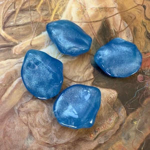 May include: Four blue, iridescent, smooth, rounded, glass stones on a brown background.