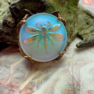 May include: A vintage iridescent glass pendant featuring a dragonfly design with gold accents. The pendant is set in a bronze-colored metal frame.