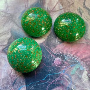 May include: Three green glass buttons with gold glitter embedded in the surface.