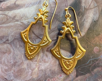 May include: A pair of gold-toned dangle earrings with intricate geometric designs. The earrings have a teardrop shape with a delicate openwork pattern.