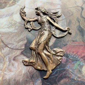 May include: A bronze-colored relief sculpture of a woman in a flowing gown, arms outstretched, holding a cluster of objects. The sculpture has intricate details and is set against a backdrop of a vintage-style print.