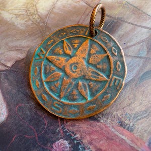 May include: A copper pendant with a turquoise patina featuring a five-pointed star with a circle in the center. The pendant is attached to a twisted copper wire loop.