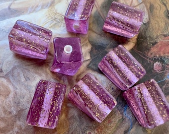 May include: Nine purple glass beads with gold flecks. The beads are rectangular and have a hole in the center for stringing.