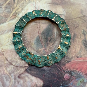 Może przedstawiać: Okrągły, teksturowany pierścień z metalu w kolorze zielonym i złotym z falistym brzegiem.