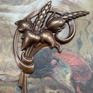 May include: A bronze-colored metal wall decor featuring a stylized floral design with a curved stem and three flower buds. The design is reminiscent of Art Nouveau style.