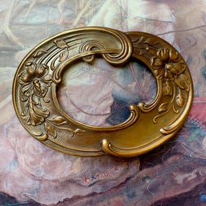 May include: A gold-toned metal frame with an oval shape and intricate floral designs. The frame has a smooth, polished finish and is perfect for adding a touch of vintage elegance to any project.