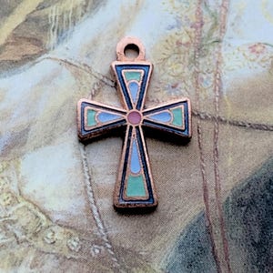May include: A copper-toned cross pendant with a loop at the top for hanging. The cross features a colorful enamel design with blue, green, and pink accents. The pendant is likely for jewelry or religious use.