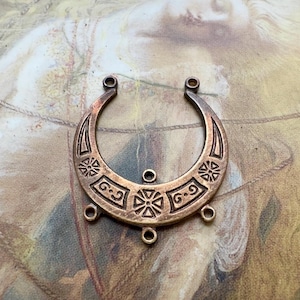 May include: A copper-colored crescent-shaped jewelry component with decorative etched patterns. The design includes floral and geometric motifs, with multiple holes for attachment. Ideal for crafting earrings, pendants, or other jewelry pieces.