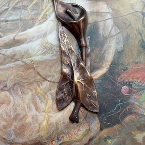 May include: A bronze sculpture of a calla lily with a single leaf. The sculpture is detailed and realistic, with a smooth, polished finish.