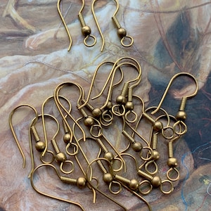 Puede incluir: Un grupo de 10 ganchos para pendientes de color dorado con una pequeña bola en el extremo de cada gancho. Los ganchos son de metal y están diseñados para la elaboración de joyas.