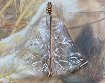 May include: A clear, bell-shaped pendant featuring an intricate, carved floral pattern on its surface. The pendant is secured by a simple copper wire wrap that extends vertically along the center, forming a small loop at the top for suspension.
