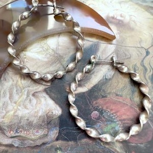 May include: A pair of silver-toned hoop earrings featuring a twisted, rope-like texture. Each circular earring is constructed with a continuous spiral design and includes a thin metal post closure at the top for securing the hoop in place.