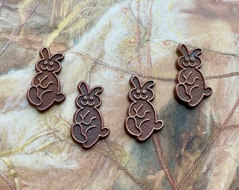 May include: Four brown ceramic bunny figurines with a smiling face. The bunnies are sitting on a brown and white textured surface.