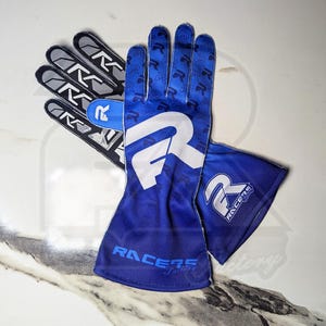 May include: A pair of blue racing gloves with white and black accents. The gloves feature a large white "R" logo on the back of the hand and the text "RACERS Factory" on the wrist. The palm of the gloves has a repeating "R" pattern.