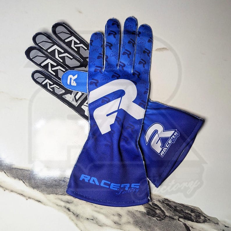 May include: A pair of blue racing gloves with white and black accents. The gloves feature a large white "R" logo on the back of the hand and the text "RACERS Factory" on the wrist. The palm of the gloves has a repeating "R" pattern.