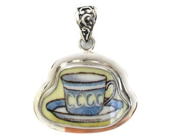May include: A silver pendant with a blue and white teacup and saucer design. The pendant is shaped like a cloud and has a silver bail.