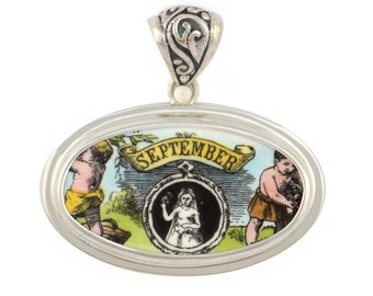 May include: Oval pendant with a silver-colored frame and bail. The pendant features a colorful illustration with the word "SEPTEMBER" on a banner. The illustration depicts cherubic figures and a central portrait of a woman.