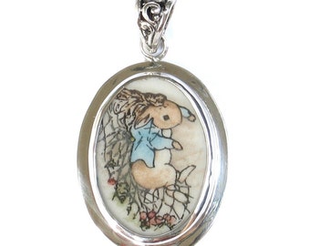May include: A silver oval pendant with a detailed image of Peter Rabbit in a blue jacket, surrounded by a delicate floral design.