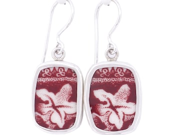 May include: A pair of silver earrings with a rectangular red and white floral design.