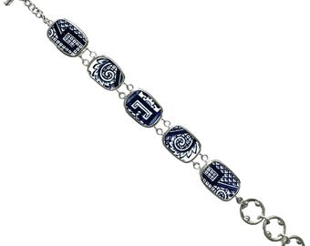 May include: A bracelet featuring five rectangular links with a white and dark blue patterned design, connected by silver-toned metal rings. The piece includes a toggle clasp at one end and a series of three circular rings at the other end.