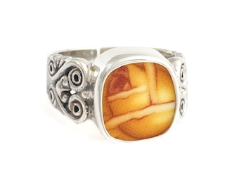 May include: A silver ring with an ornate design and a square, orange and white cameo.