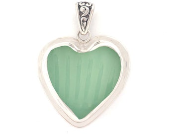 May include: A silver heart-shaped pendant with a green glass insert. The pendant has a detailed silver bail.