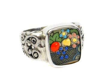 May include: A silver ring with a square, colorful, mosaic-style design featuring a fruit basket with grapes, apples, and flowers.