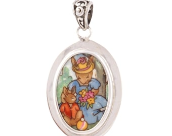 May include: Silver oval pendant with a colorful image of two rabbits. The rabbit on the left is wearing a red shirt and the rabbit on the right is wearing a blue dress and a yellow hat.