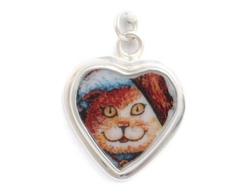 May include: A silver heart-shaped charm with a picture of a cat wearing a blue and red hat. The cat has orange fur and yellow eyes.