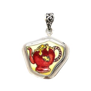 May include: A silver pendant featuring a red and yellow teapot design on a white background.
