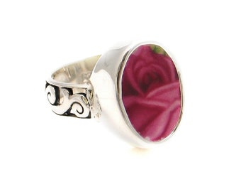 May include: A silver ring with a pink rose design set in a round bezel. The band of the ring has a decorative scroll design.