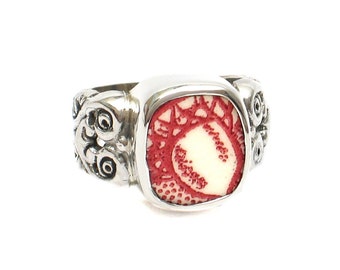 May include: A silver ring with a red and white cameo design. The ring has a square setting and intricate detailing on the band.